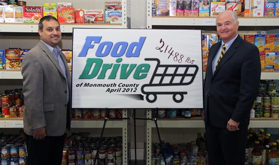 FoodBank Executive Director Carlos Rodriguez and Monmouth County Freeholder Director John P. Curley stand in front of the shelves that hold some of the 21,488 pounds of food donated in April's Food Drive of Monmouth County.